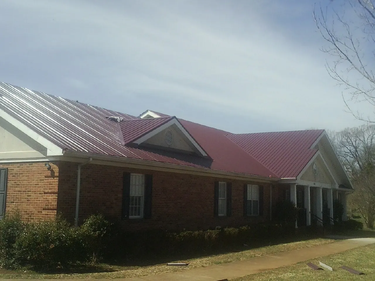 Red metal roof with gabled entries on a long brick building, from a Hail Damage Roof Repair job in Triadelphia