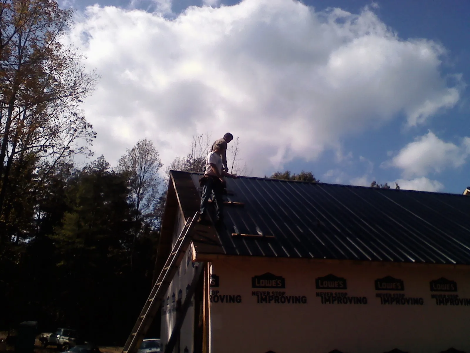 Roofer fastening dark metal panels high against a cloudy sky, from a Roof Inspection job in Triadelphia