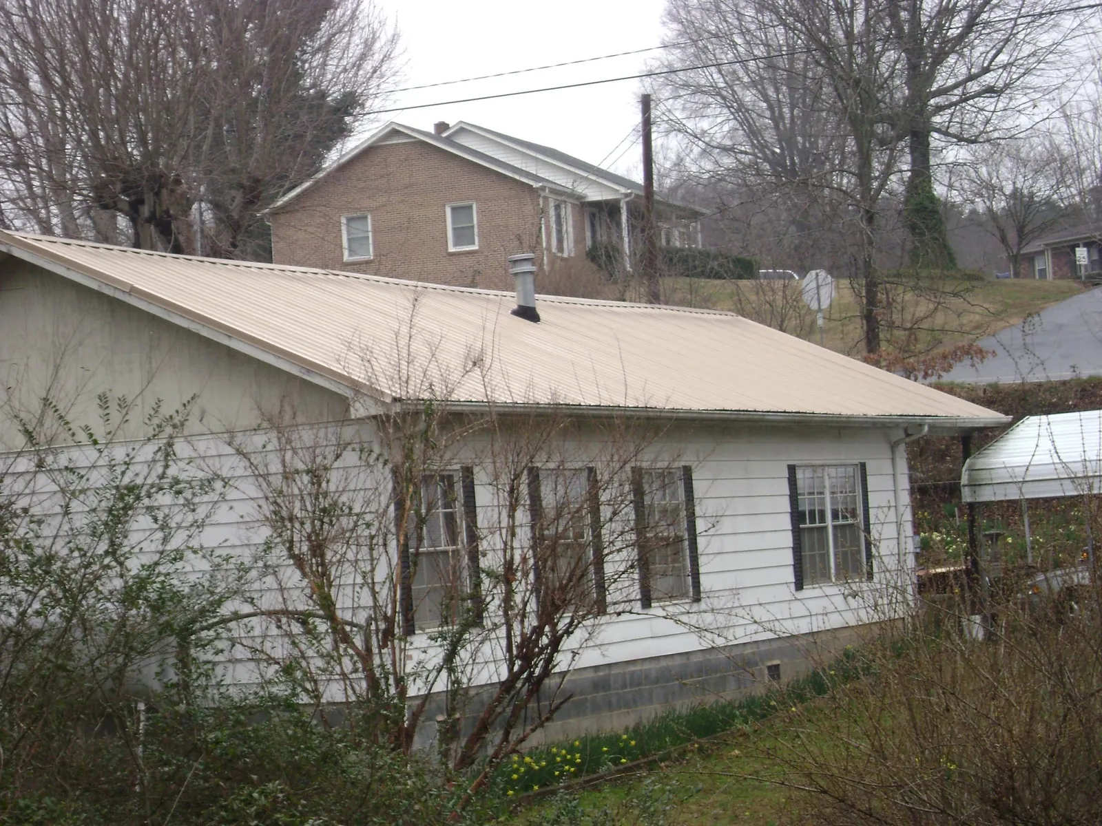 Tan metal roof on a white sided house set into a hillside — Commercial Roofing by Roofing Brothers in Triadelphia